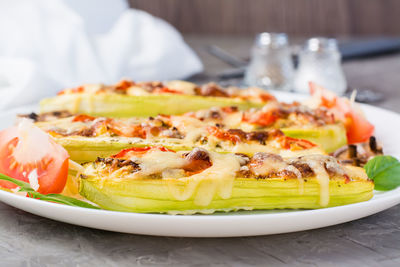 Ready-to-eat baked zucchini halves stuffed with cheese and tomato on a plate on the table. 