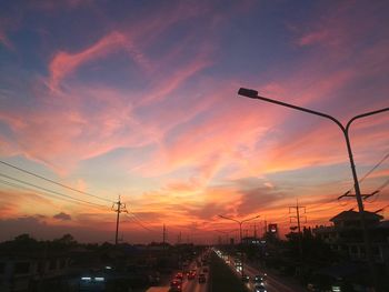 Cars on street against dramatic sky during sunset