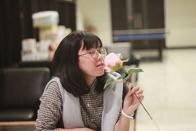 Young woman holding flower while sitting at home