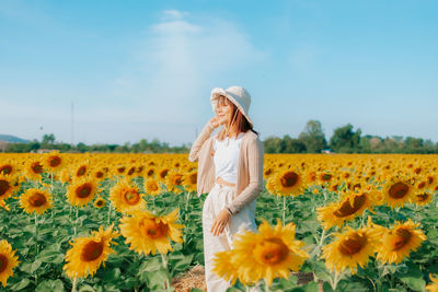 Woman standing on sunflower field against sky