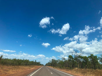 Empty road amidst trees on field against sky