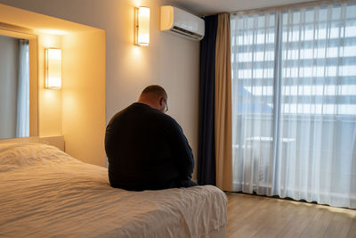 Rear view of woman looking through window at home