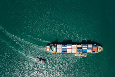 Aerial top view container ship and tugboat dragging floating in green sea, business and industry 