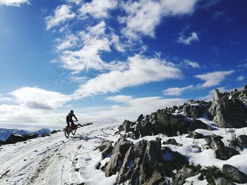 Rear view of man riding bicycle on snowcapped mountain against sky