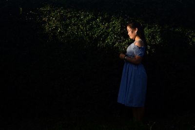 Side view of young woman standing by plants at night