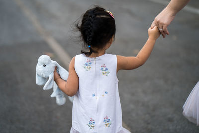 Girl holding dog doll walking at street with mum