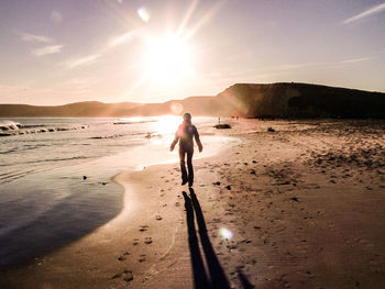 Woman walking on beach against sky during sunset