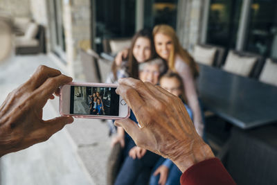 Cropped hands of senior man photographing family through smart phone on porch