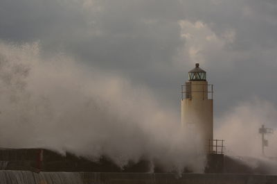 Lighthouse by building against sky