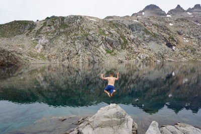 Rear view of man on rock by lake