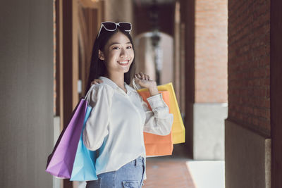 Smiling young woman holding shopping bag standing against wall