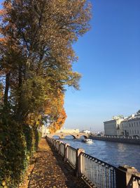 Footpath by river against clear blue sky during autumn