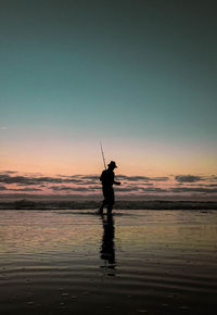 Silhouette man fishing in sea against sky during sunset