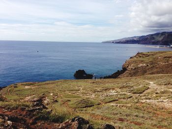 Grassy mountains by sea against cloudy sky