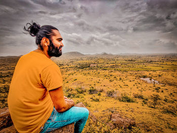 Side view of young man sitting on land