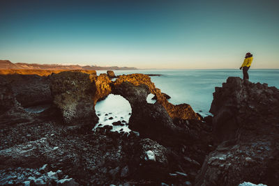 Man standing on rock by sea against sky