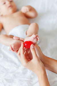 Mother holds newborn baby's feet. tiny fingers and red massage ball in woman's hand. cozy morning.