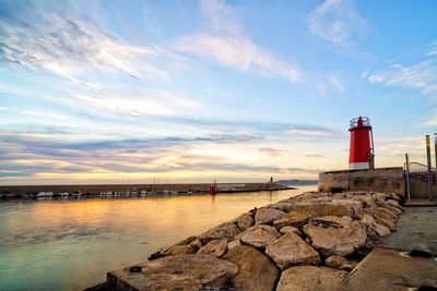 Lighthouse by sea against sky during sunset