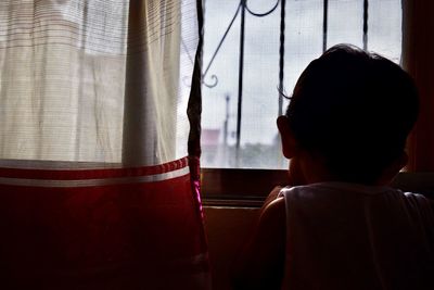 Rear view of boy looking through window