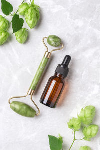 Unbranded serum bottle, face roller with hop on marble background. jade face roller 