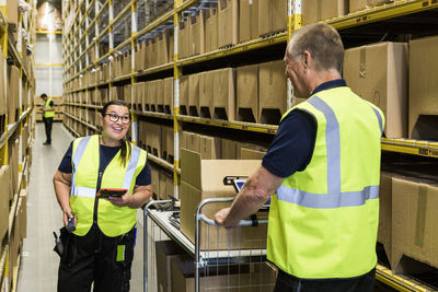 Smiling coworkers discussing while standing on aisle amidst racks at distribution warehouse