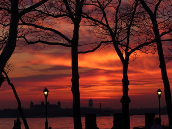 Silhouette bare trees by sea against orange sky