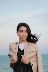 Portrait of young woman standing in sea against sky