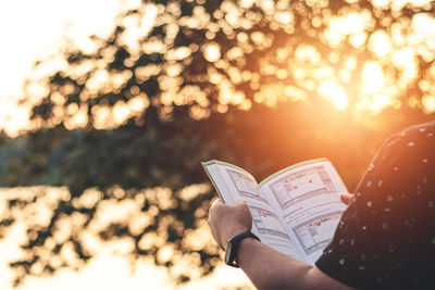 Midsection of person reading book against bright sun