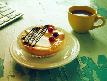 High angle view of coffee cup and tart with computer keyboard on wooden table