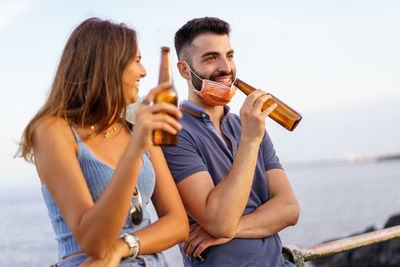 Coronavirus couple of best friends making a beer at sunset talking and laughing holding face masks