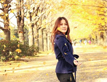 Portrait of smiling young woman standing against trees during autumn