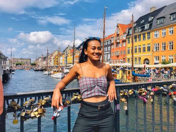 Thoughtful young woman smiling while standing against canal in city