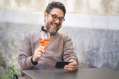 A middle-aged man toasts at a virtual party in a video call with a spritz during the quarantine