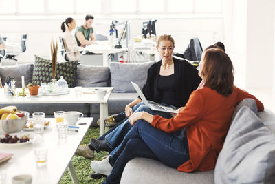 Businesswomen with laptop discussing project on sofa in office lobby