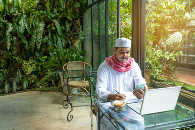 Full length of man using mobile phone while sitting on table