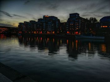 River by illuminated buildings against sky at dusk