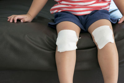 Midsection of boy sitting on sofa with bandage on knees