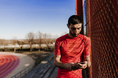 Athlete using mobile phone while standing by sports track