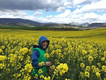 Cheerful boy standing on rapeseed field against cloudy sky