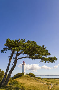 Lighthouse and trees on field against sky