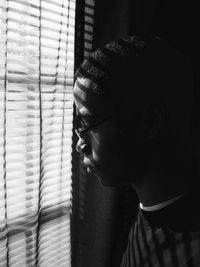 Side view of man looking through window blinds in darkroom