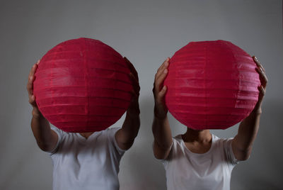 People covering faces with red paper lanterns against wall
