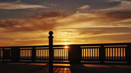 Silhouette man standing by railing against sky during sunset