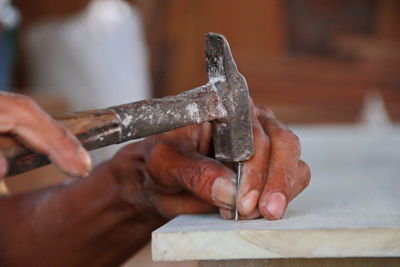 Cropped hand hammering nail on wooden plank