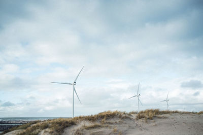 Wind turbines on the dunes of the north sea against cloudy sky