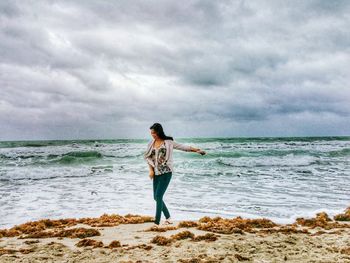 Woman walking on seashore at against cloudy sky