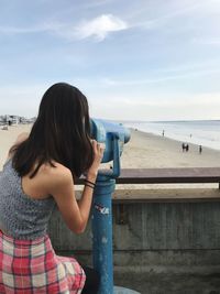 Rear view of woman looking through coin-operated binocular at beach