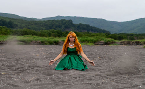 Woman playing with sand at beach against sky