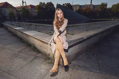 Young woman sitting on retaining wall in city