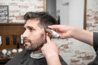 Cropped hand of barber trimming hair of customer